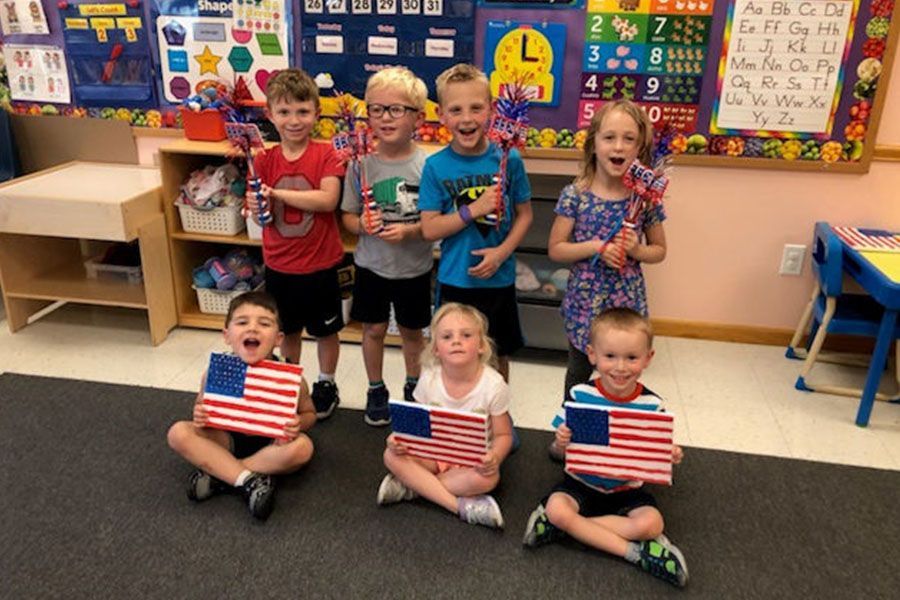 A group of children are holding american flags in a classroom.