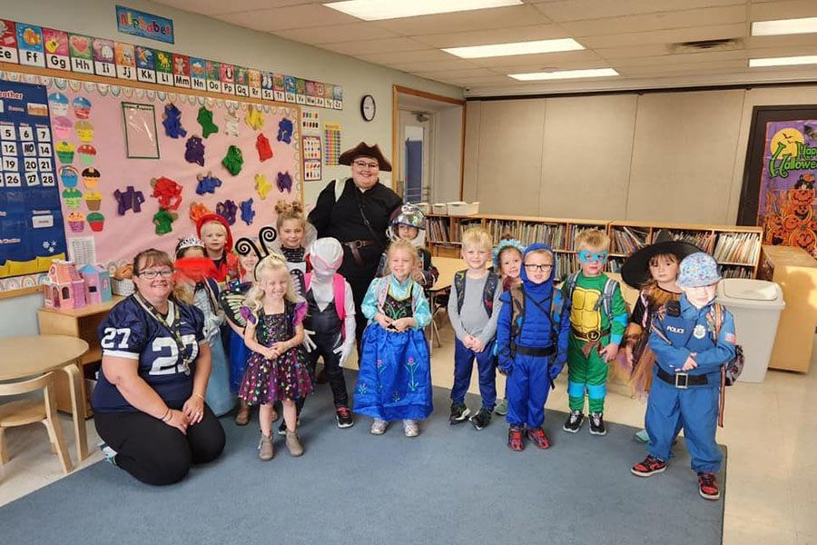 A group of children in costumes are posing for a picture in a classroom.