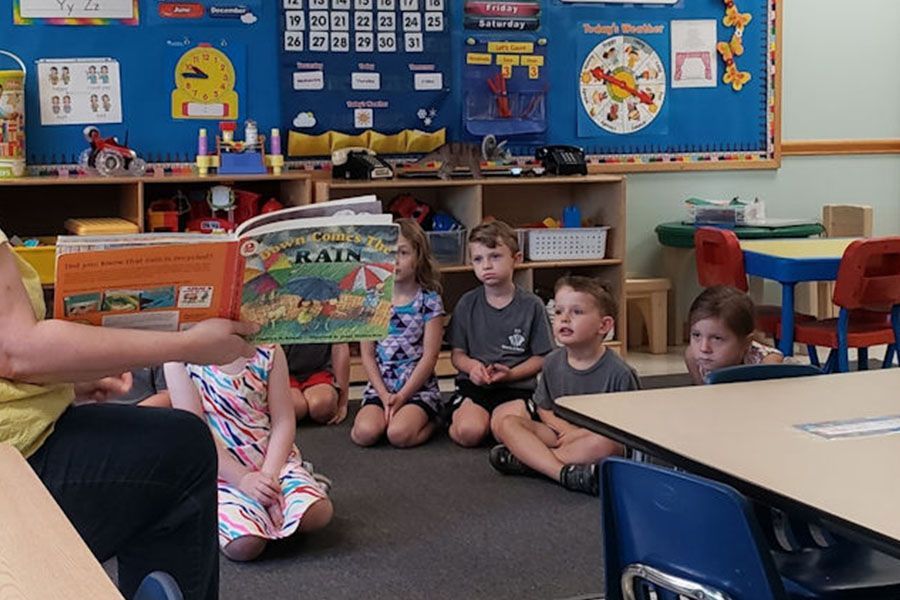 A woman is reading a book to a group of children in a classroom