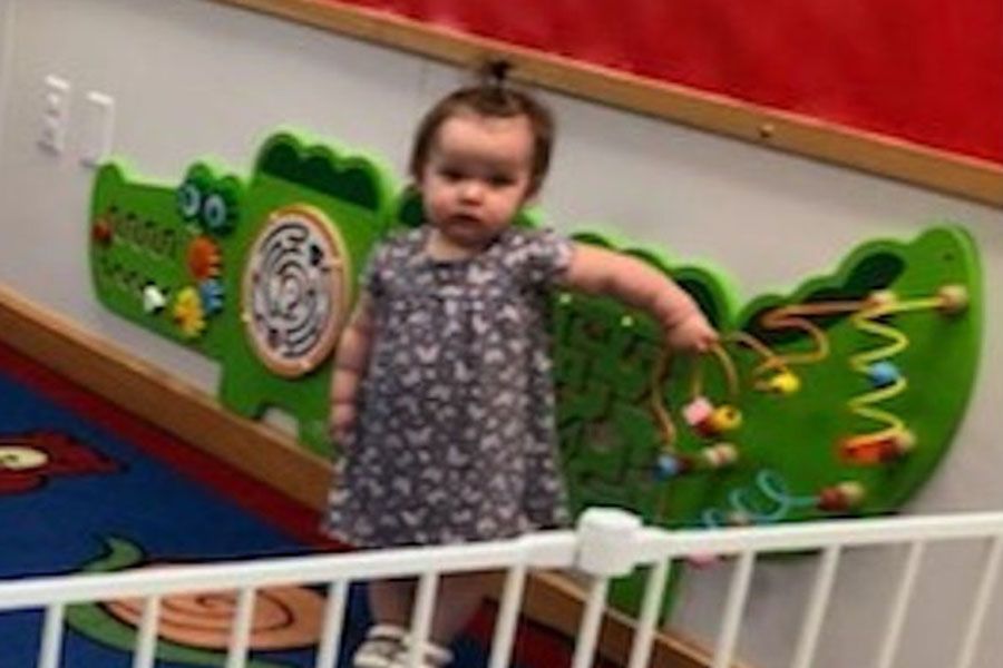 A little girl is standing in front of a wall with toys on it.