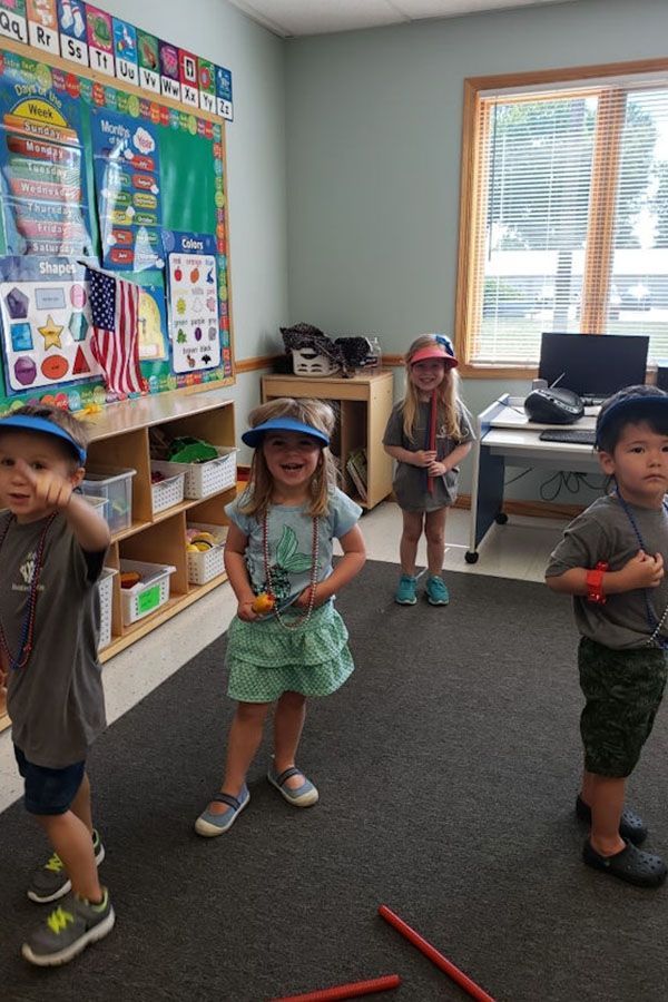 A group of children are standing in a classroom wearing hats.