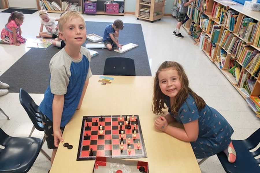 A boy and a girl are sitting at a table playing chess.