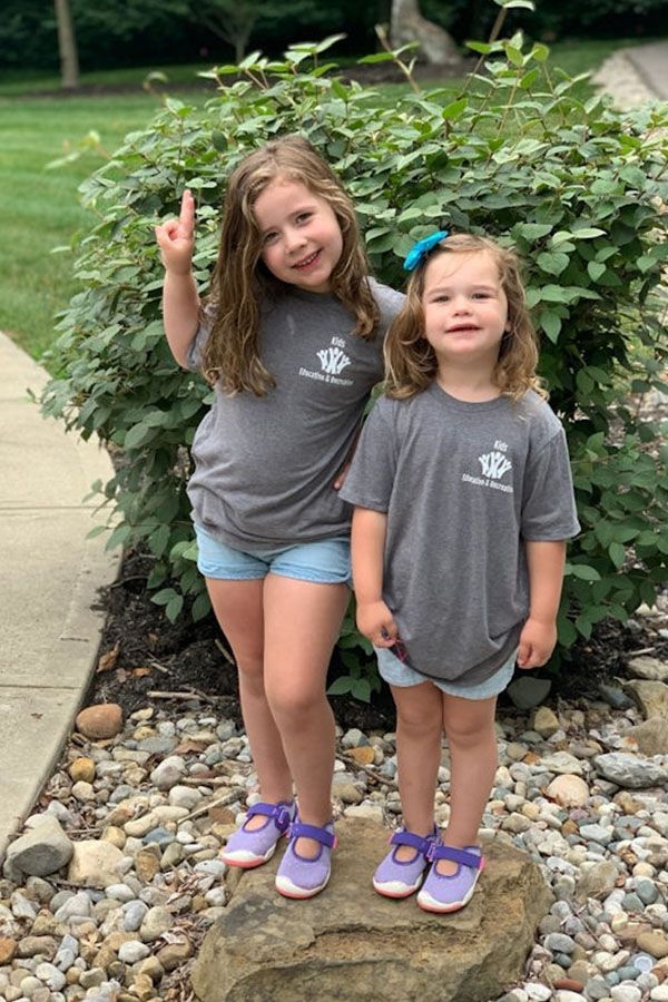 Two little girls are standing next to each other on a rock.
