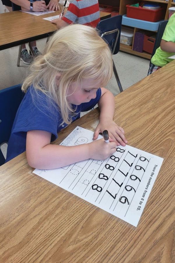 A little girl is writing on a piece of paper in a classroom.
