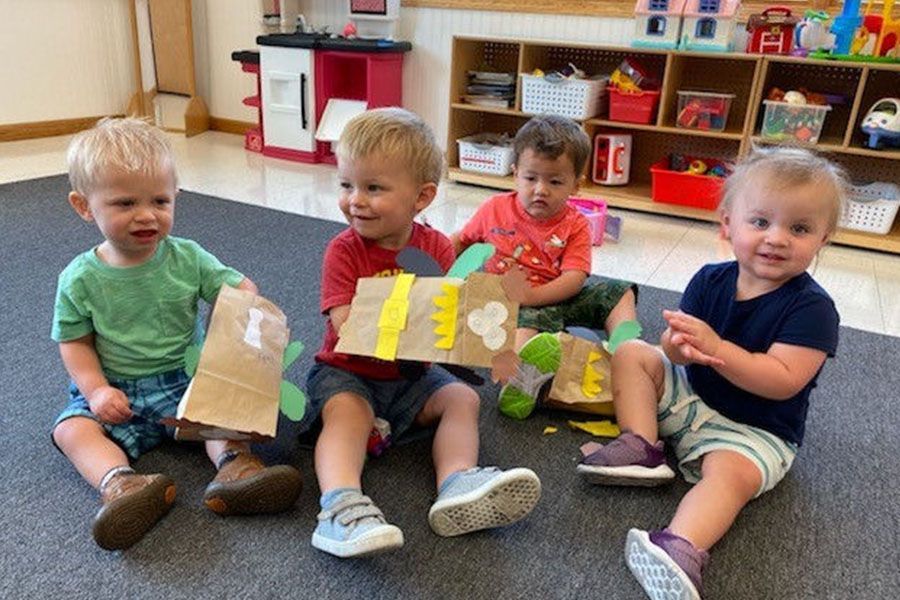 A group of young children are sitting on the floor holding crafts.