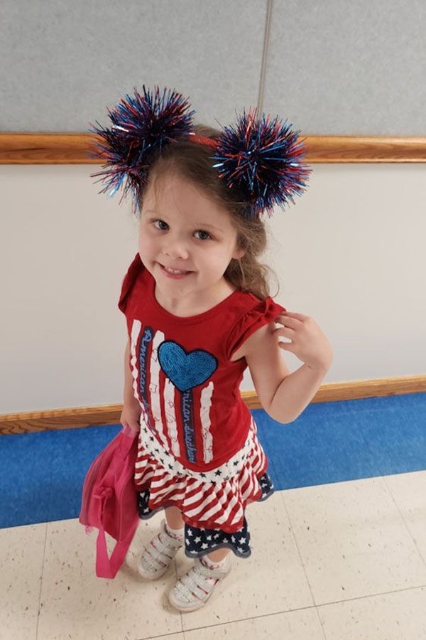 A little girl wearing a red white and blue outfit with pom poms in her hair