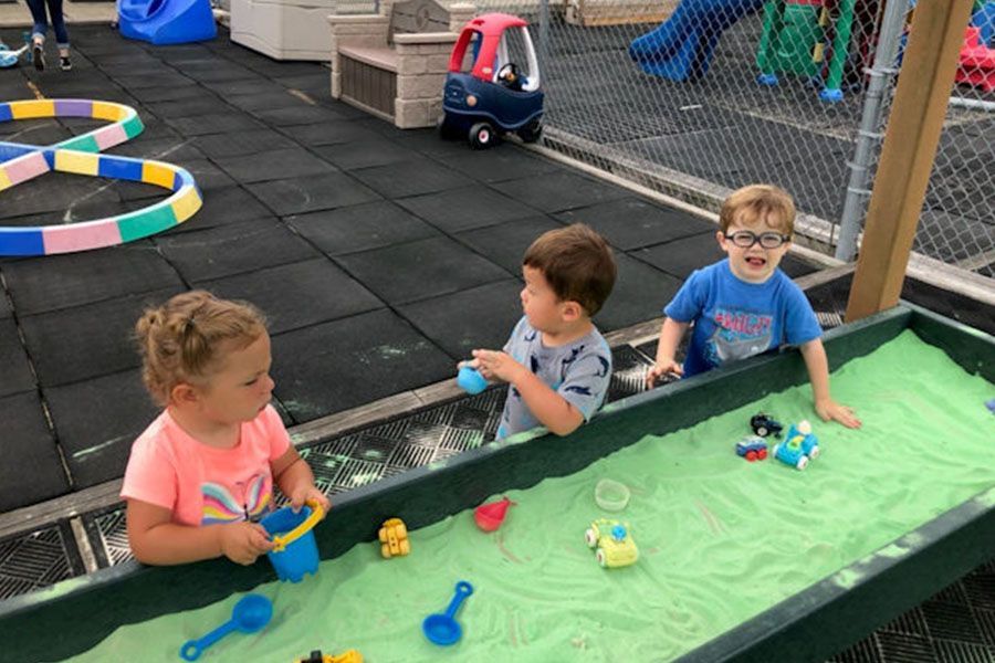 Three children are playing in a sandbox with toys.