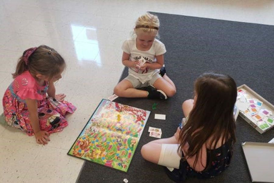 Three little girls are sitting on the floor playing a game.