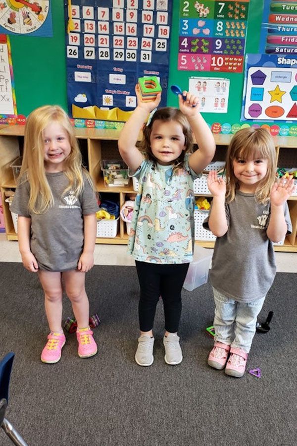 Three little girls are standing next to each other in a classroom.