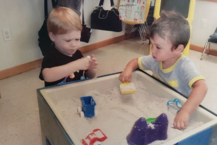 Two young boys are playing with toys in a sandbox with the letter b on it