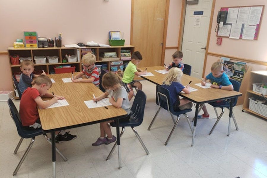 A group of children are sitting at tables in a classroom
