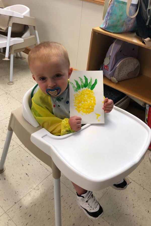 A baby is sitting in a high chair holding a drawing of a pineapple.