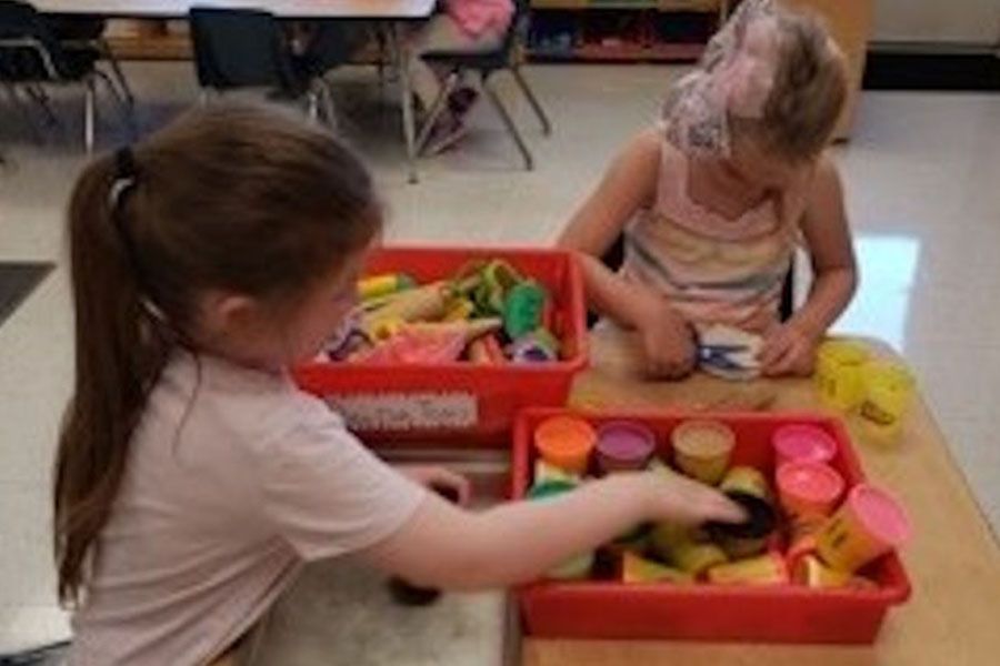 Two young girls are playing with play dough in a classroom.