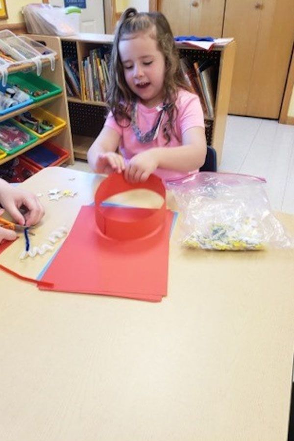 A little girl is sitting at a table playing with a red object
