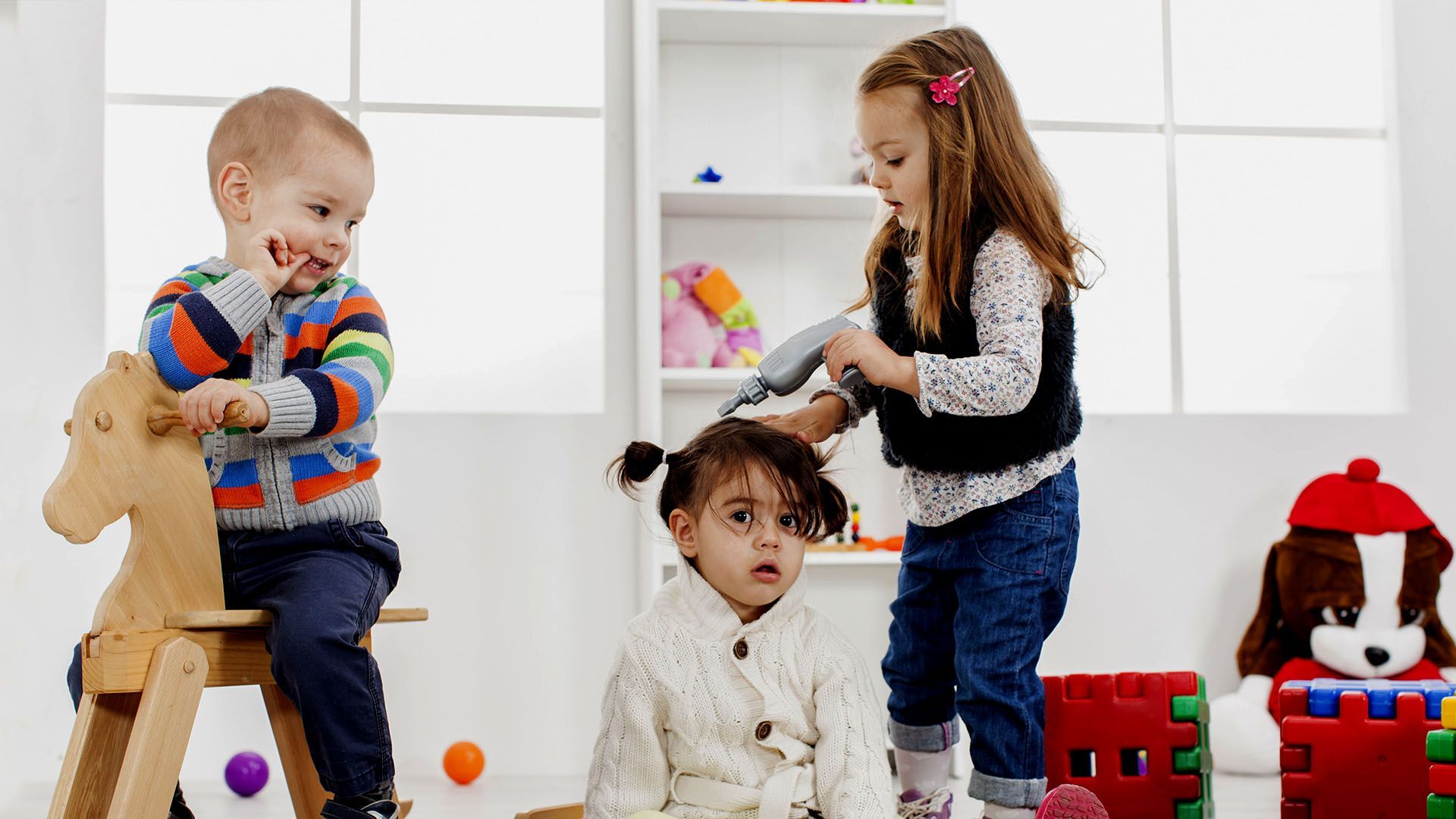 Three children are sitting on the floor playing with colorful balls.