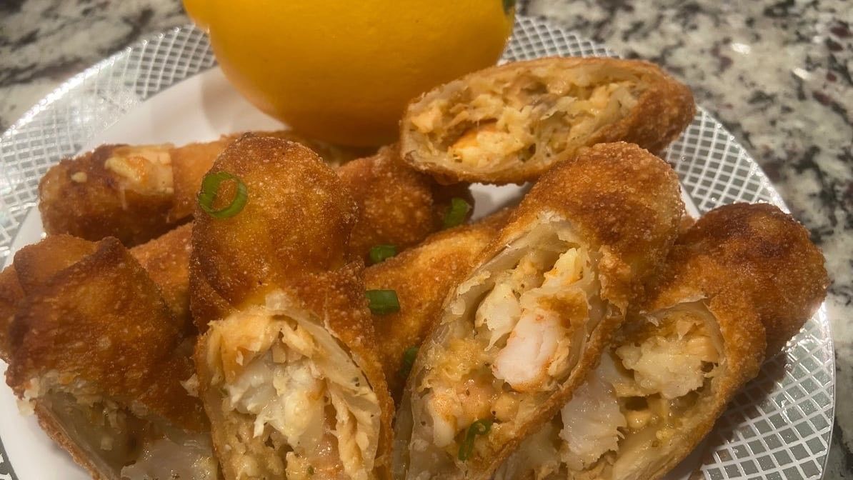 A plate of egg rolls with a glass of orange juice on a table