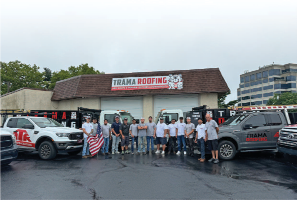 Group of people posing in front of a Tamal Roofing building with trucks parked on wet pavement