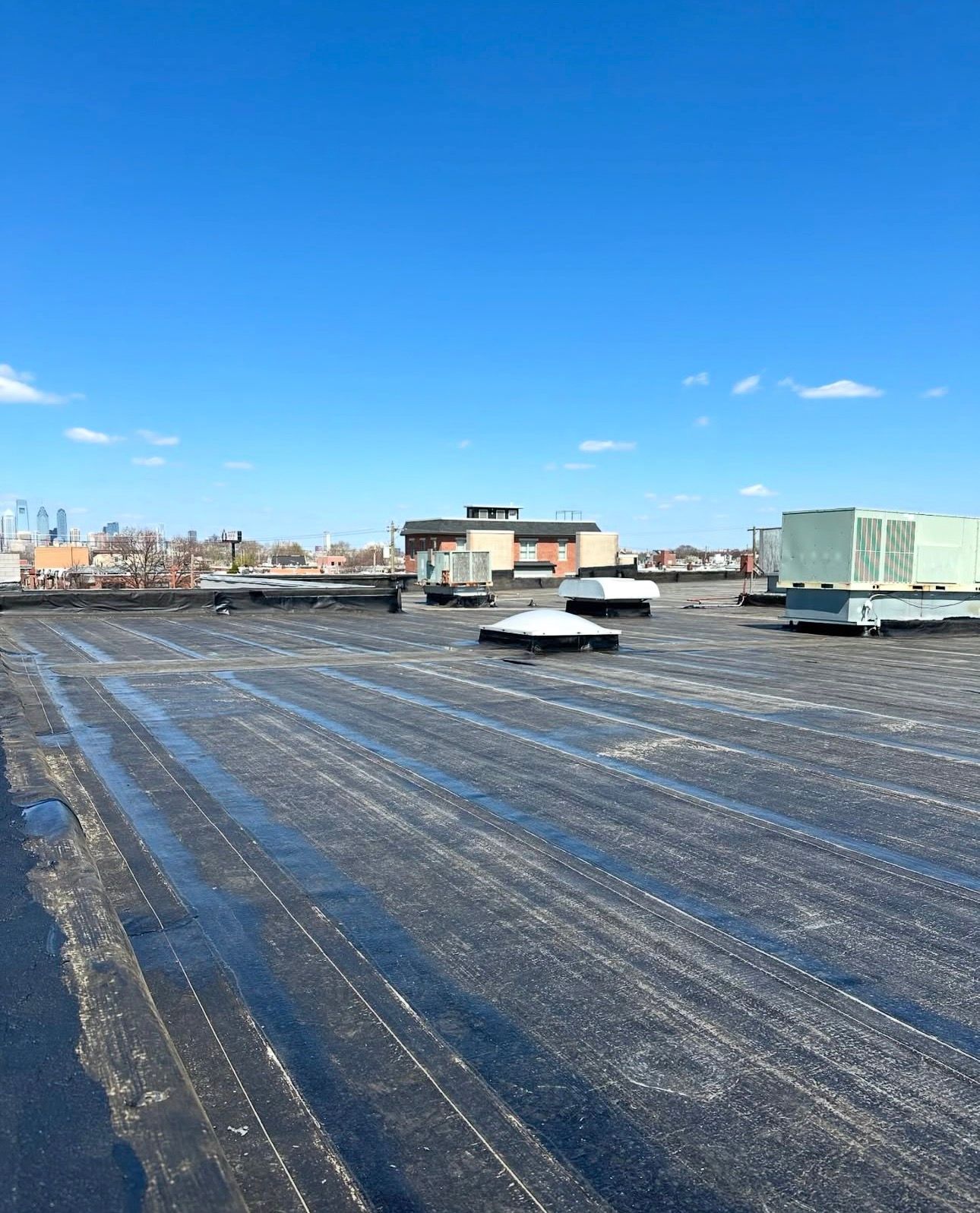 Rooftop with snow patches and HVAC units under a clear blue sky, city skyline in the distance