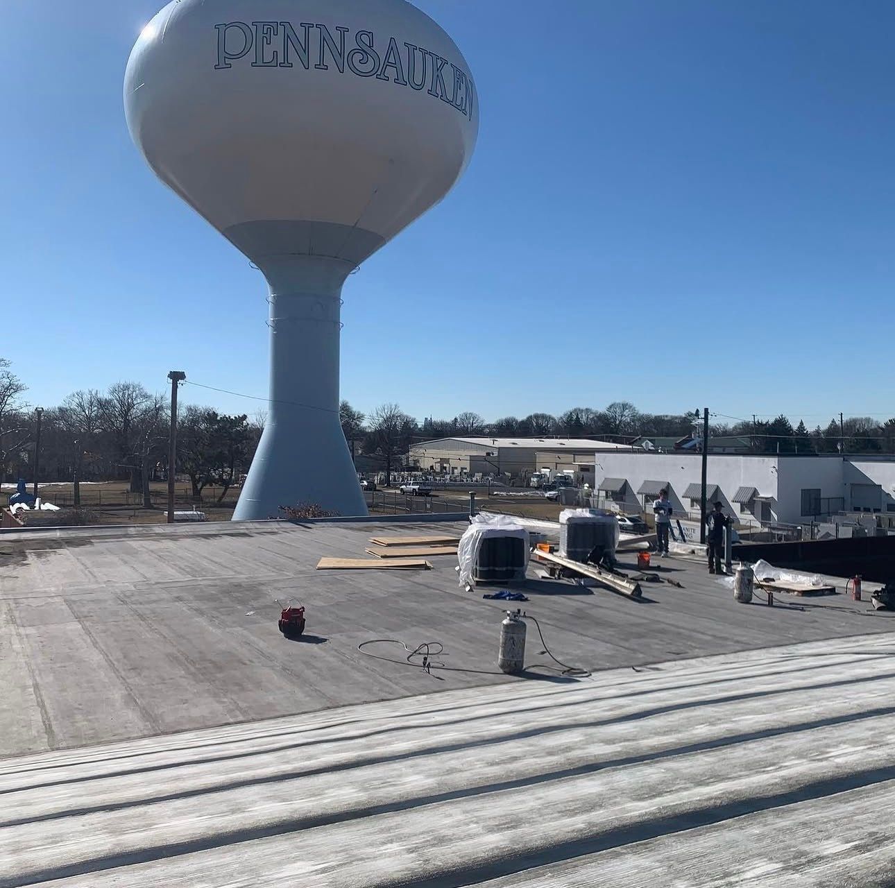 Water tower on a flat rooftop with workers and equipment under a clear blue sky