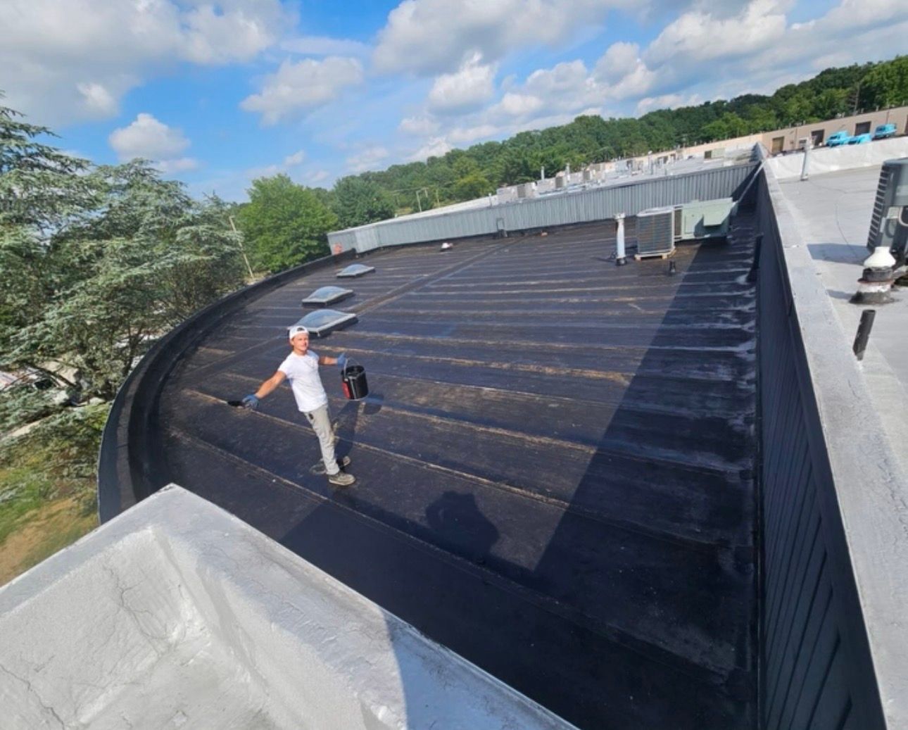 Worker on a black rooftop membrane near a white parapet under a blue sky.
