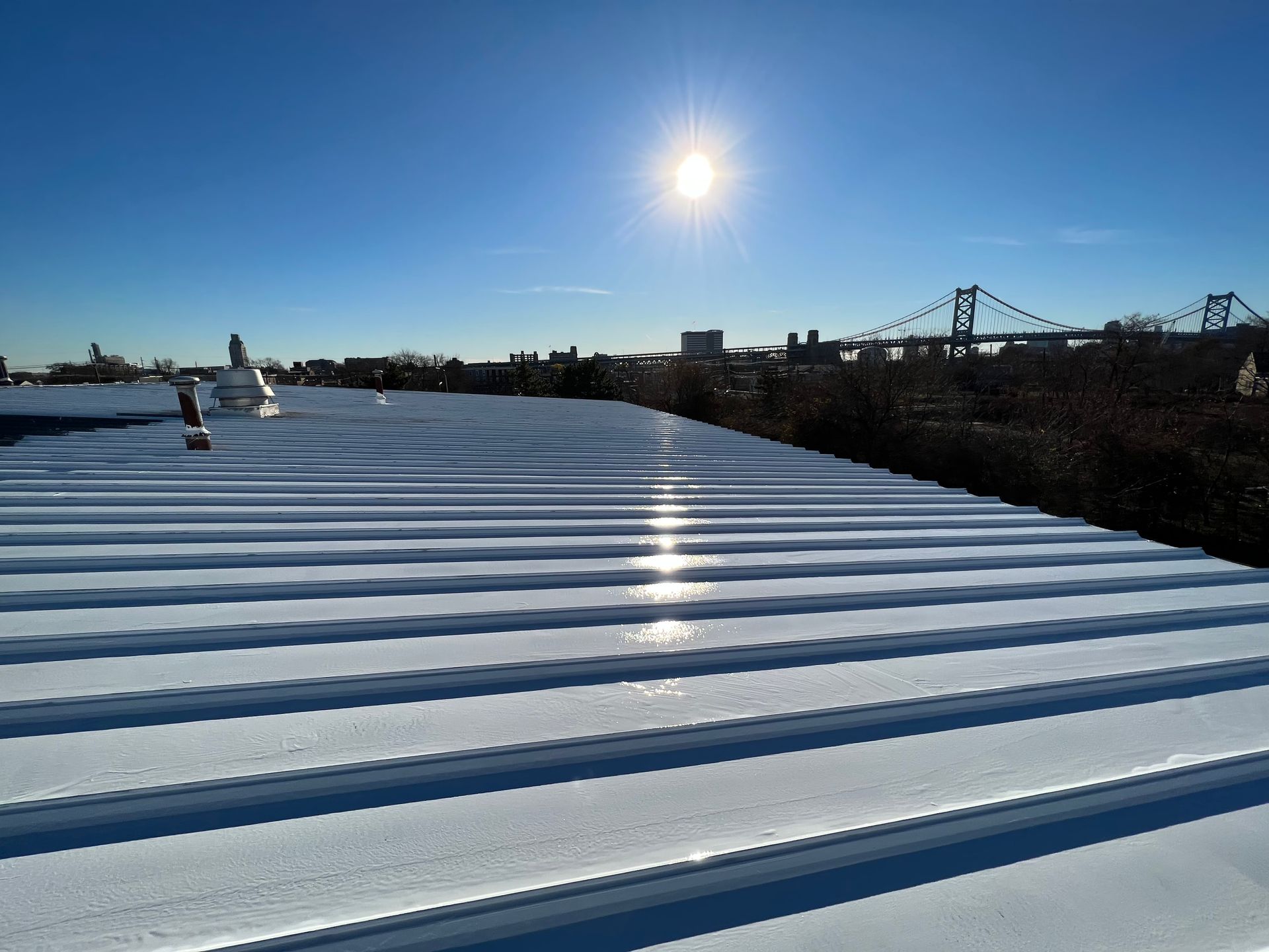 Sunlit corrugated metal roof with blue sky and distant industrial structures at the horizon