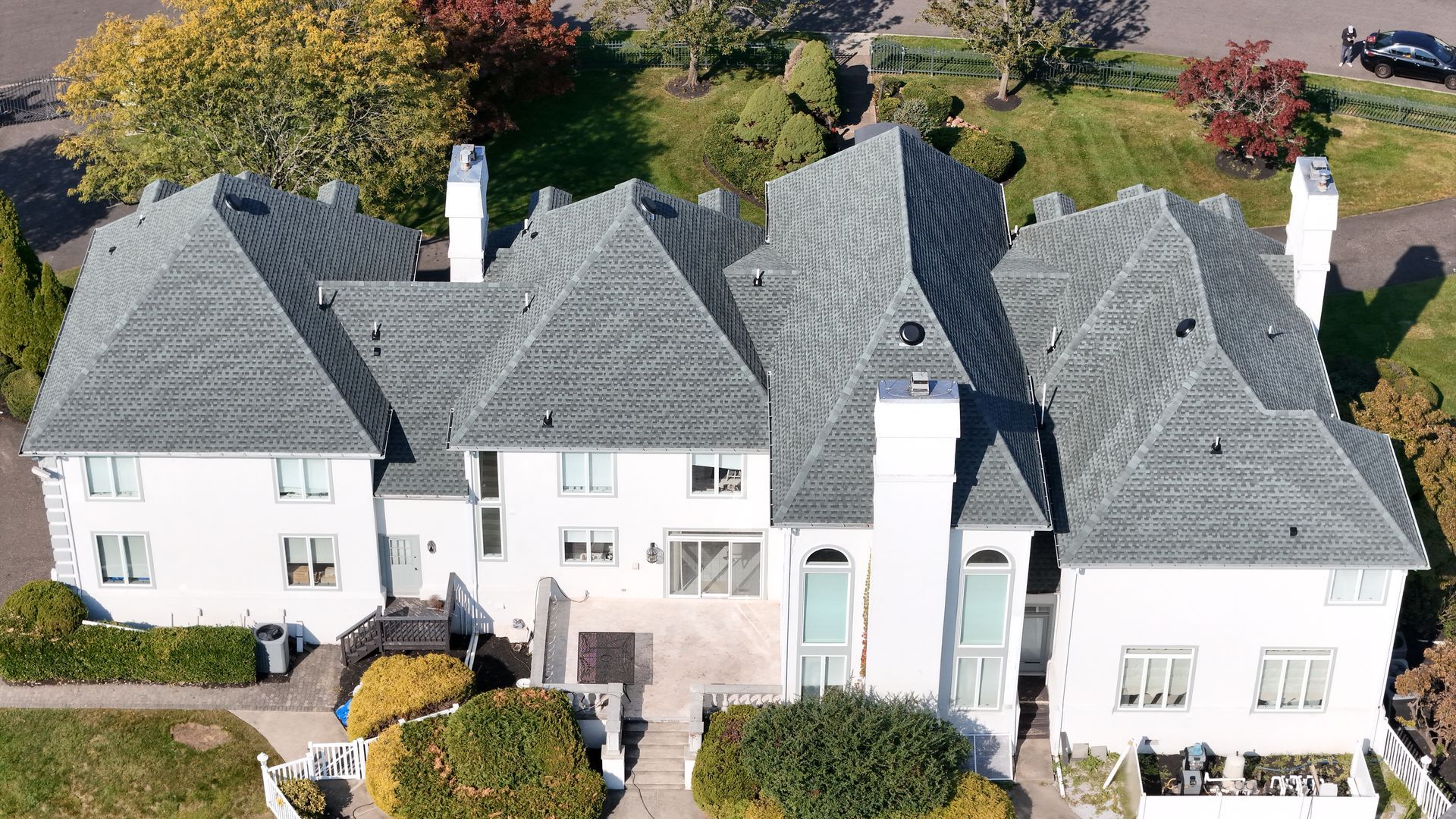 Aerial view of a large white house with gray roofs and surrounding autumn trees.