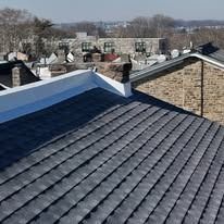 Rooftop with dark gray shingles and snow, overlooking a neighborhood on a clear day