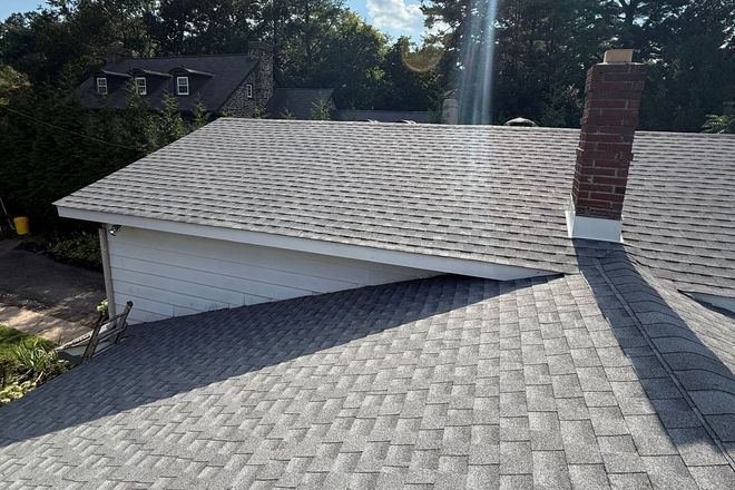 Roof with gray shingles, a brick chimney, and a white garage in bright sunlight