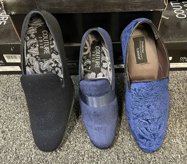Three pairs of men's slip-on dress shoes: black, blue with a strap, and blue with embroidered design.