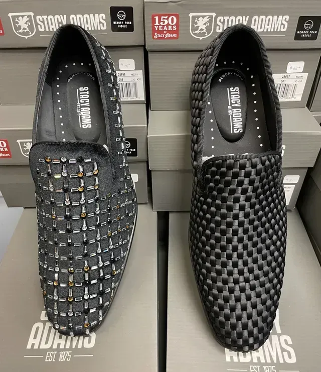 Two black Stacy Adams woven slip-on shoes on gray shoeboxes, one with studded accents.