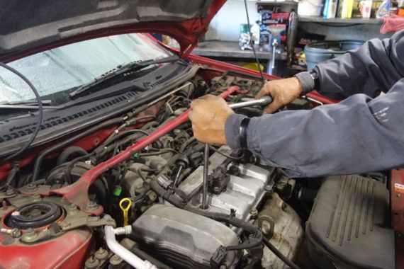 A man is working on the engine of a red car.