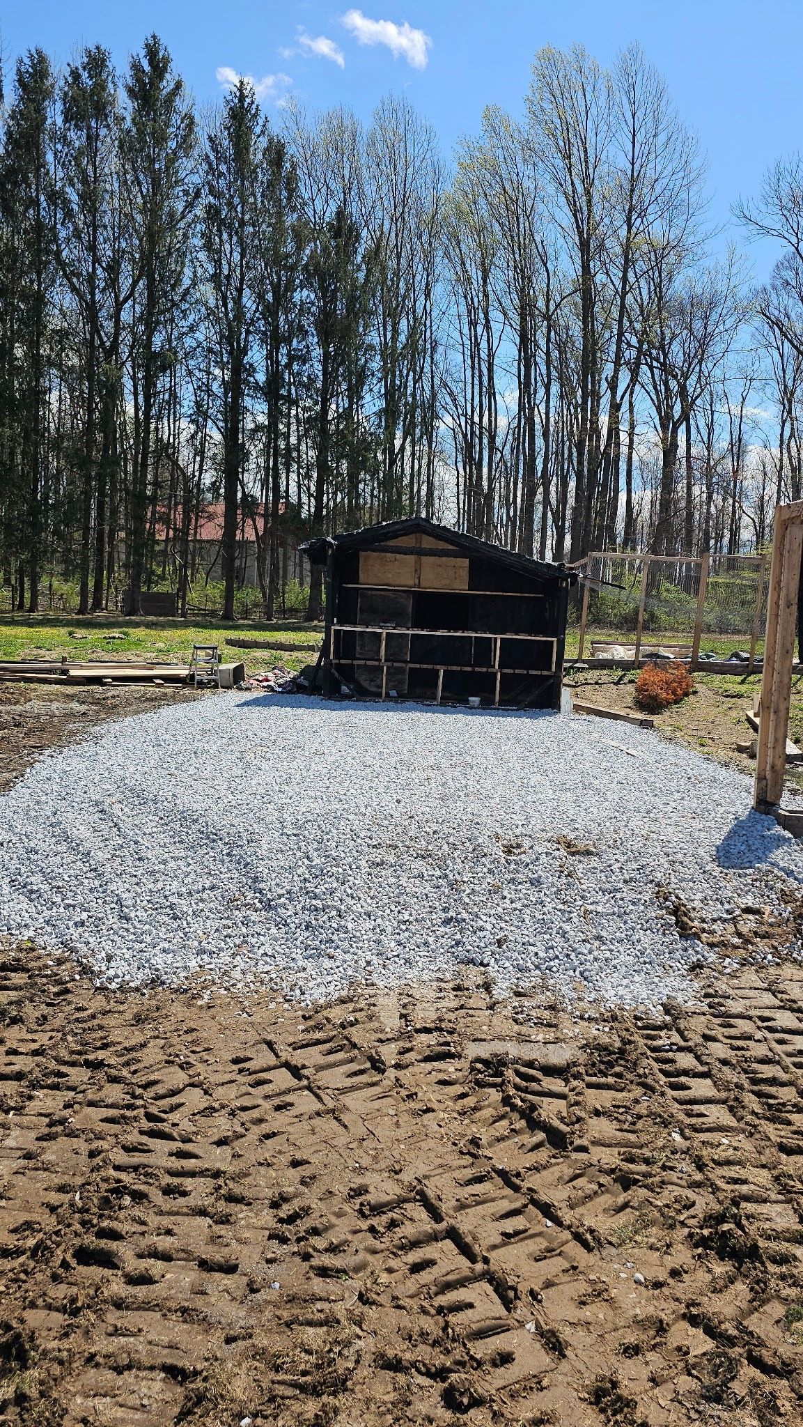 A pile of gravel is sitting in the middle of a dirt field with trees in the background.