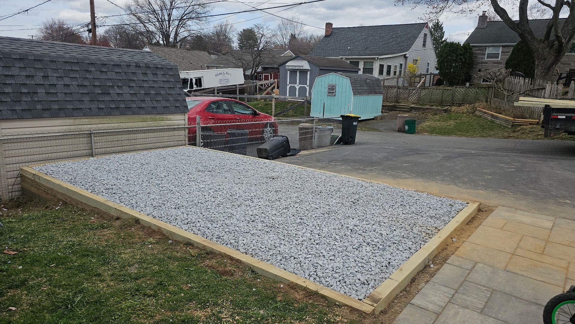 A red car is parked in a driveway next to a pile of gravel.