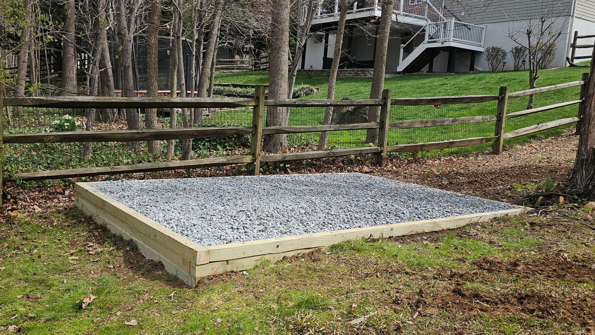 A wooden fence surrounds a gravel area in front of a house.