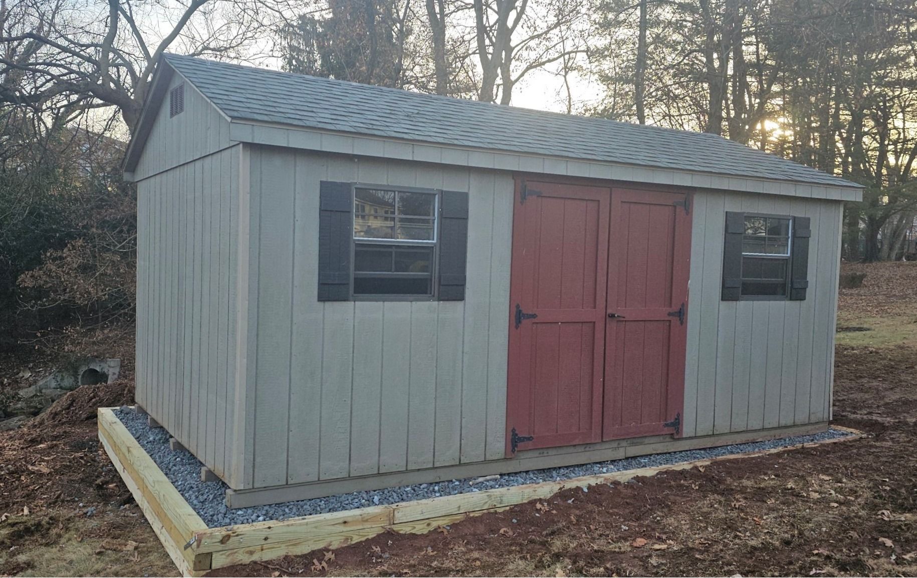 A shed with a red door and black shutters is sitting in the backyard
