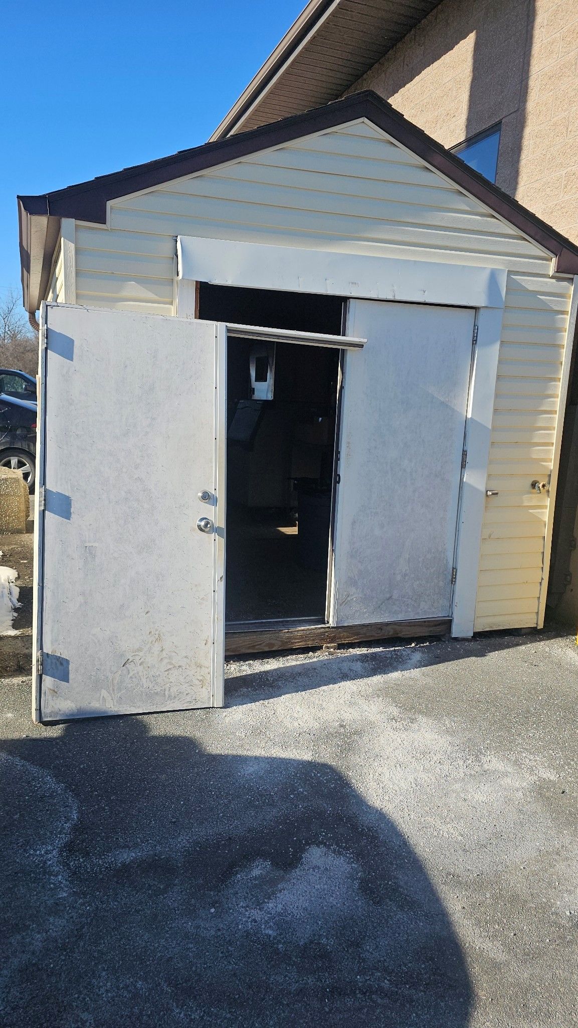 A shed with its doors open is sitting next to a house