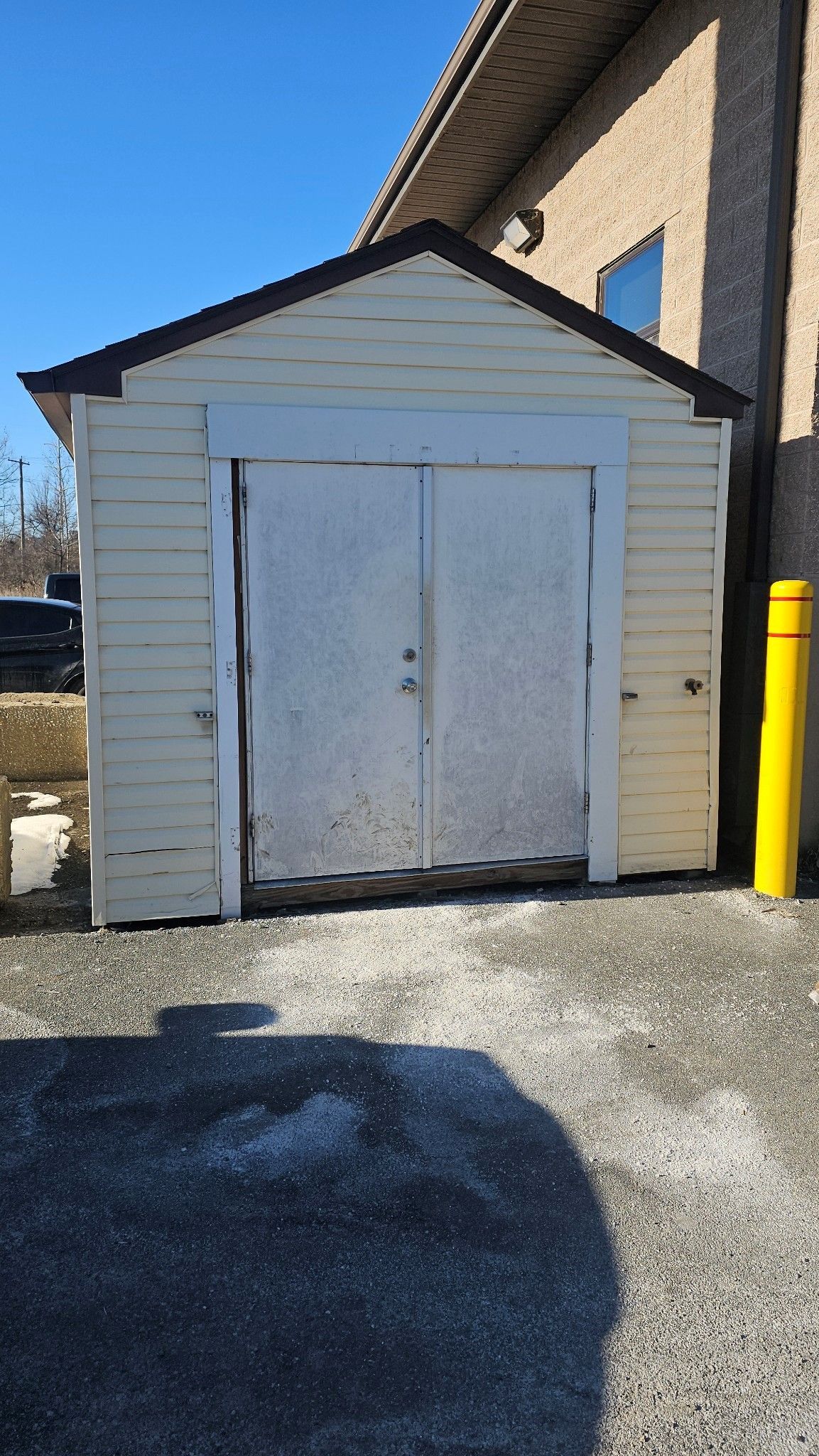 A white shed with a brown roof is sitting next to a yellow pole