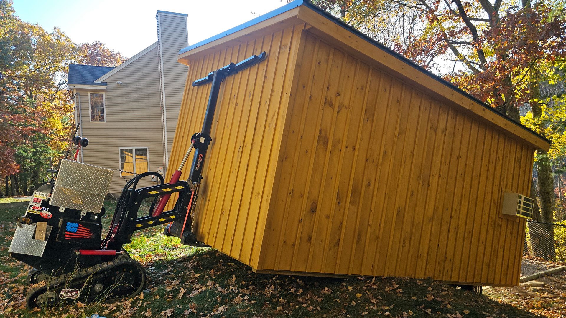 A yellow shed is being lifted by a tractor in front of a house.