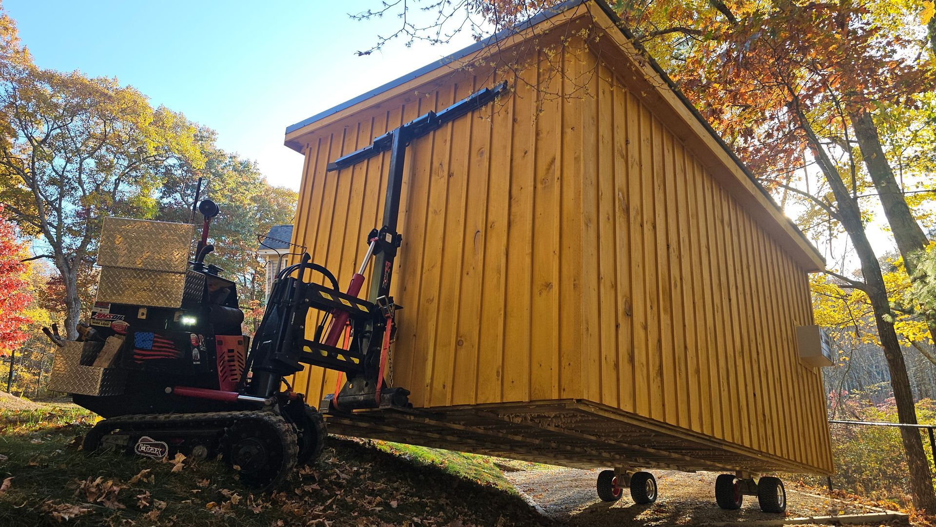 A large wooden shed is being lifted by a forklift.