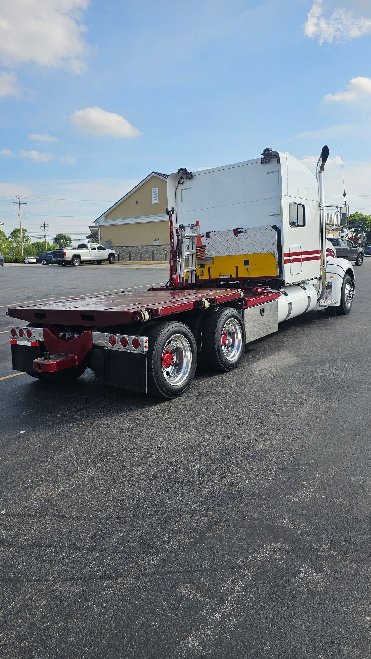 A semi truck with a flatbed trailer is parked in a parking lot.