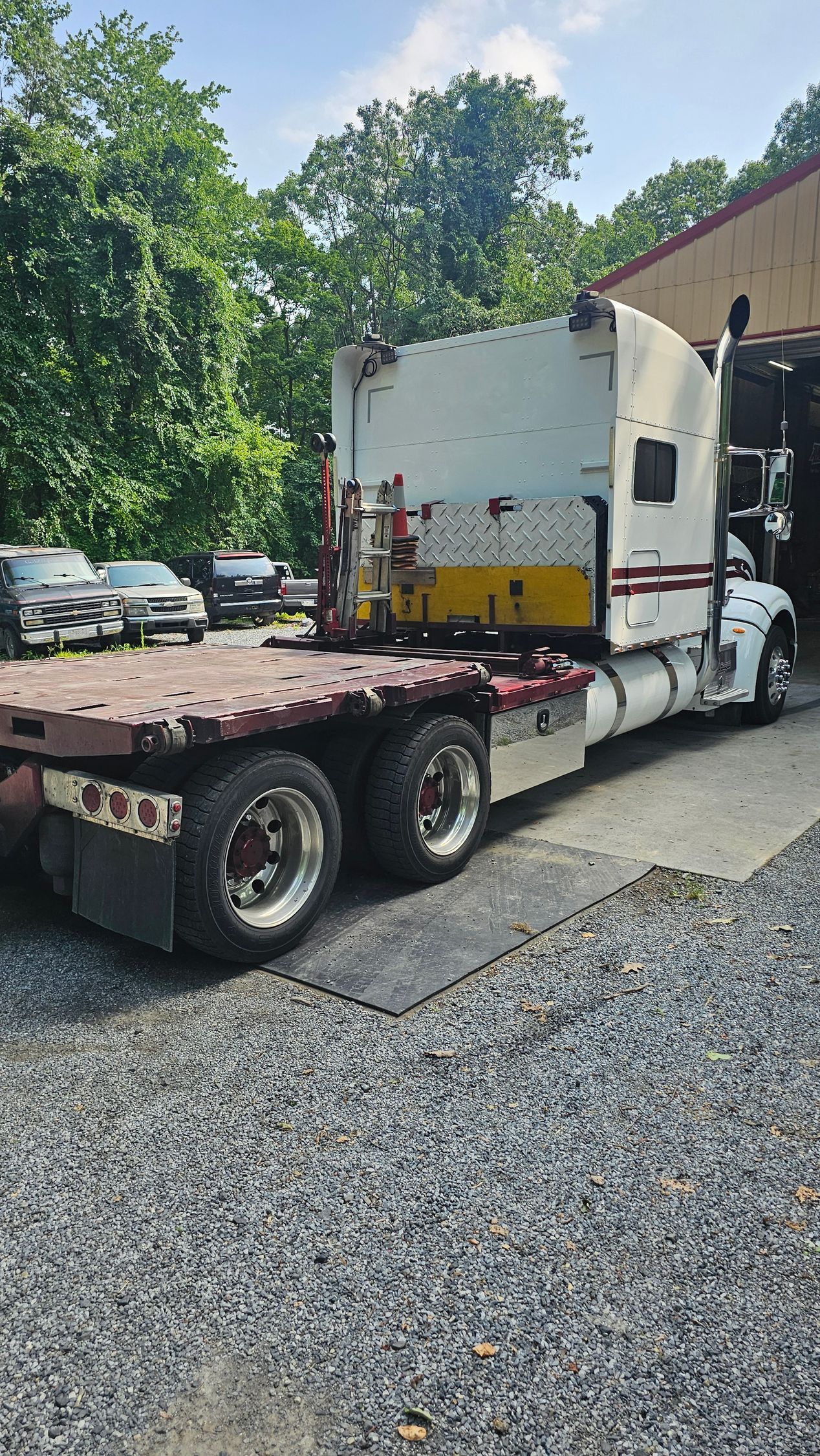 A semi truck is parked in a gravel lot in front of a garage.
