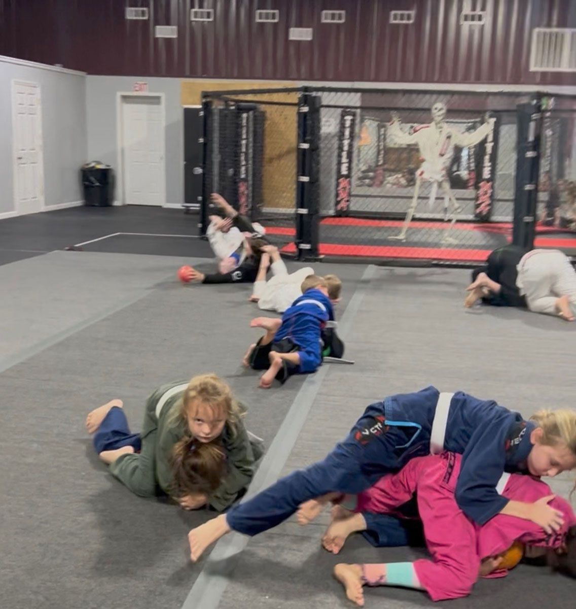 Children in martial arts uniforms practice grappling on mats