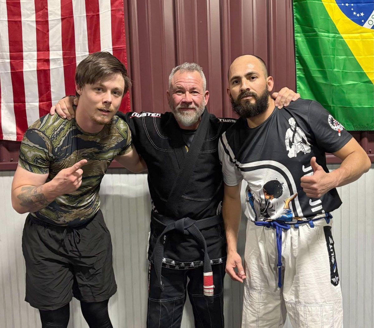 Three men in a gym with flags of USA and Brazil in the background