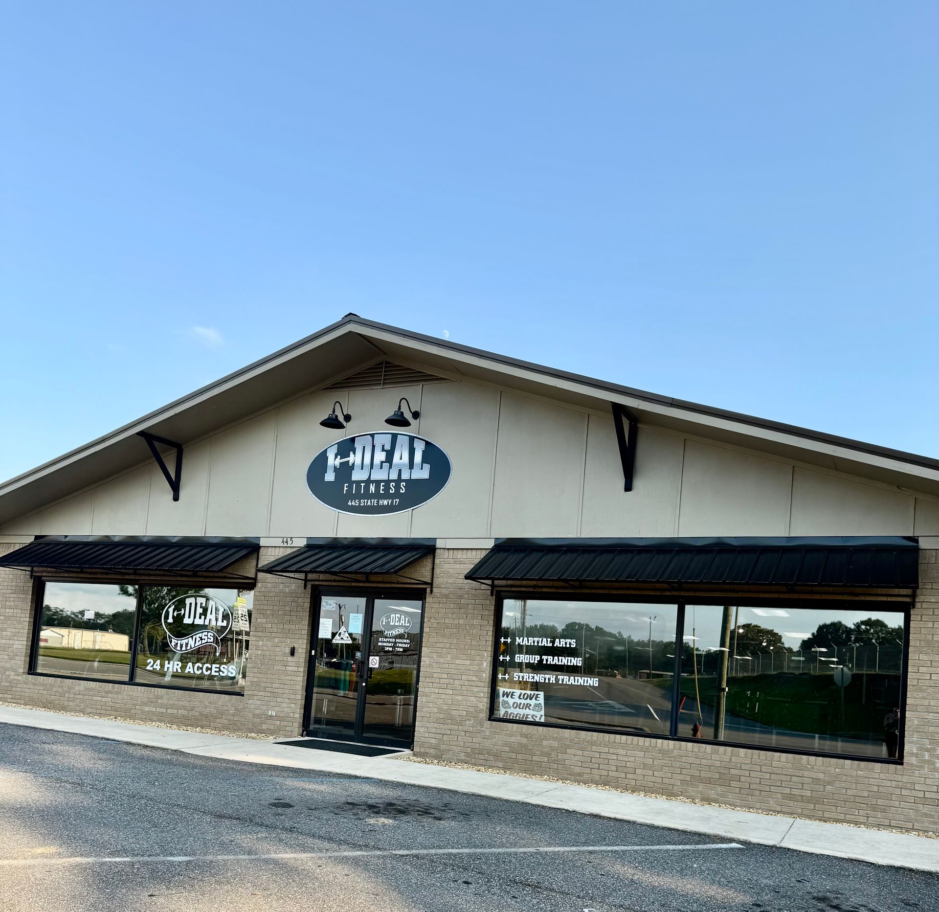 Exterior of a business with black awnings and a logo above the door under a light blue sky. The building is brick with reflective windows.