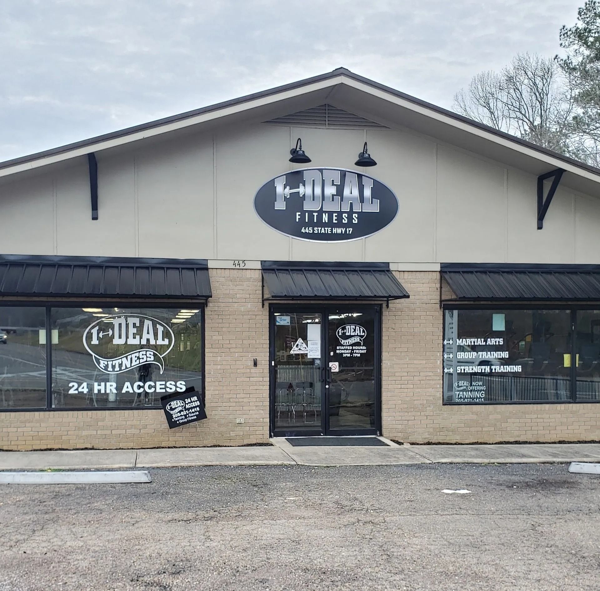 Exterior of Ideal Fitness gym with black awnings, sign, and 24-hour access notice.