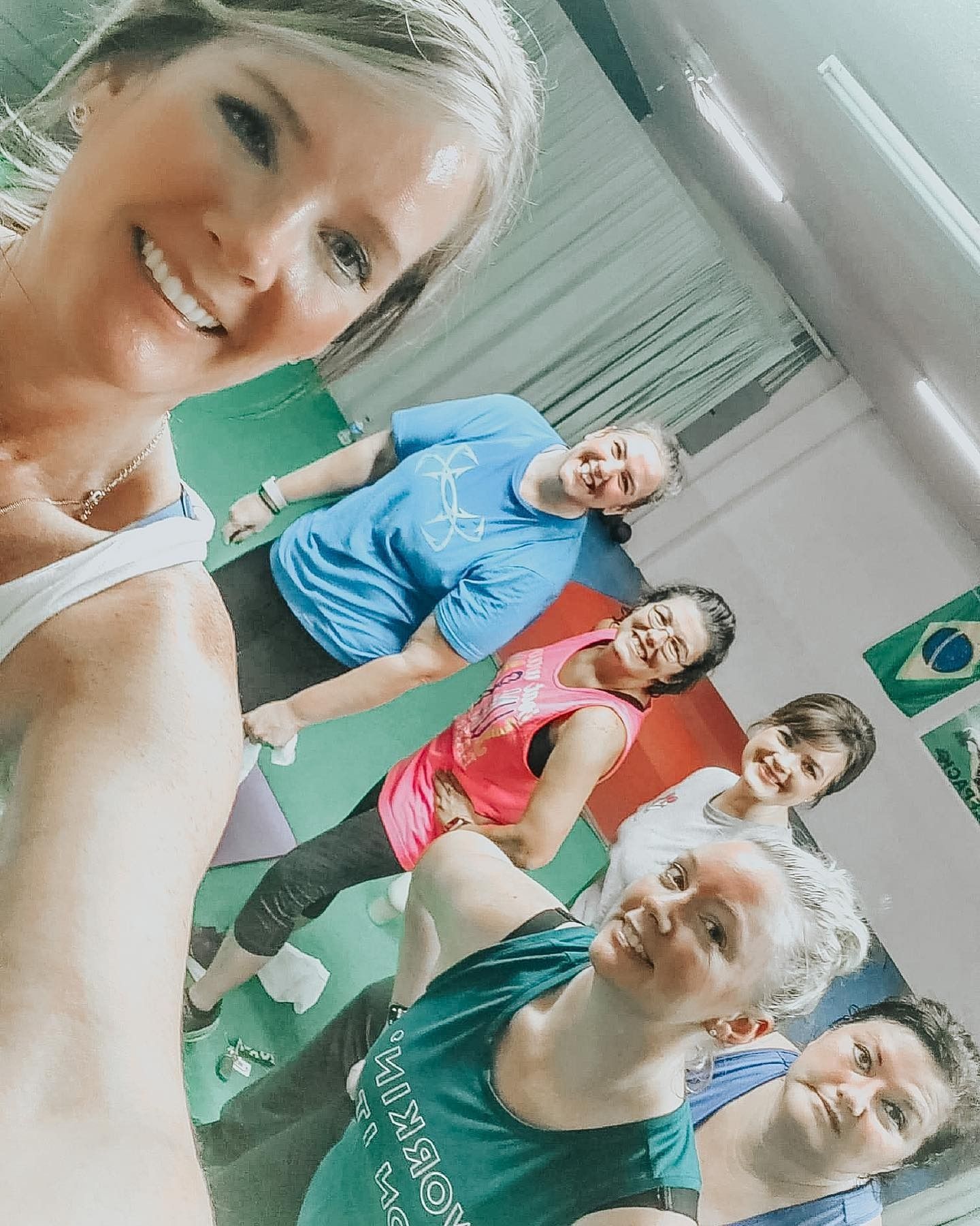 Group of smiling women taking a selfie in a gym, some wearing athletic clothing.