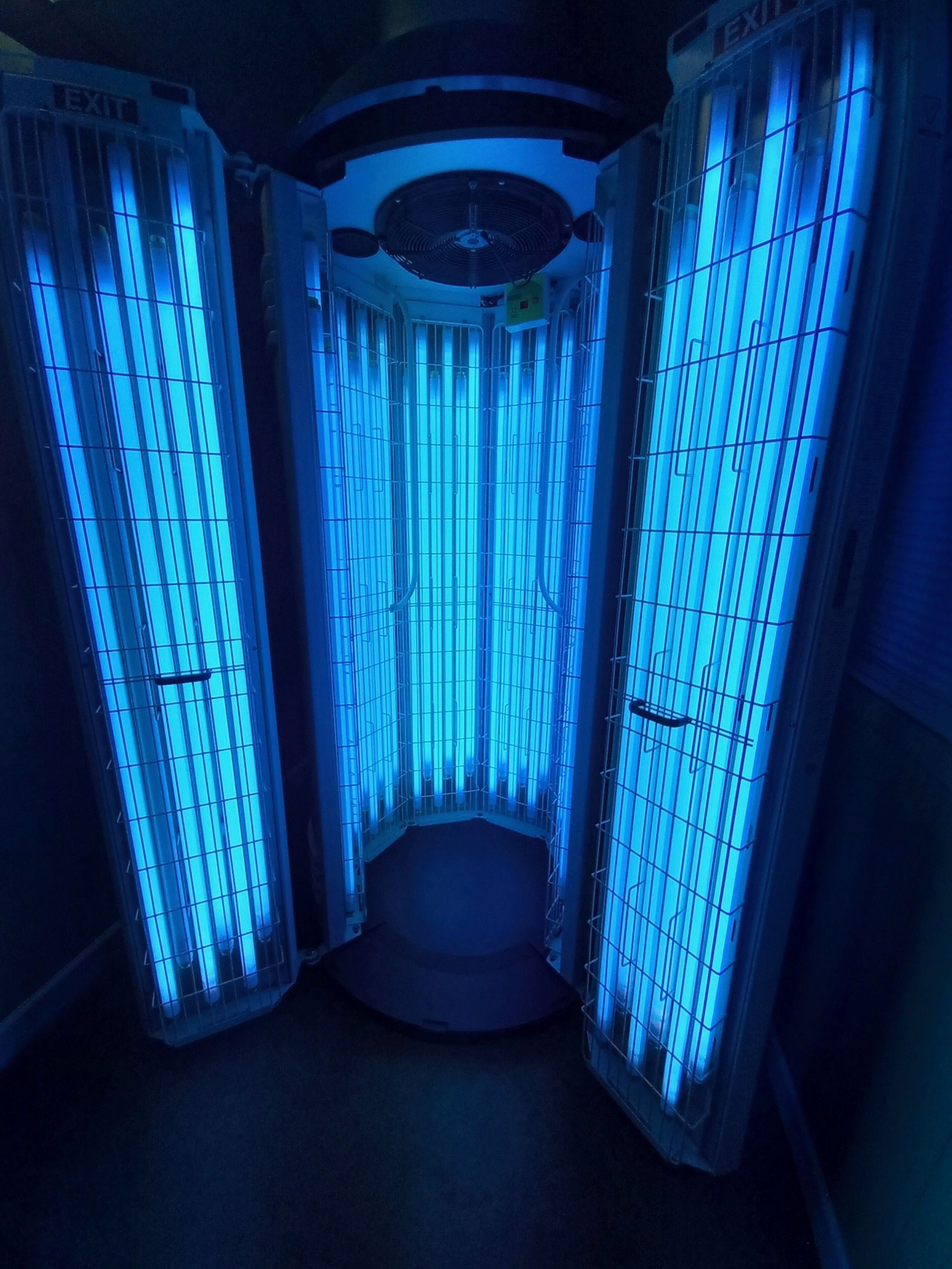 Tanning bed with bright blue UV lights. The bed is open and empty, ready for use, in a dark room.