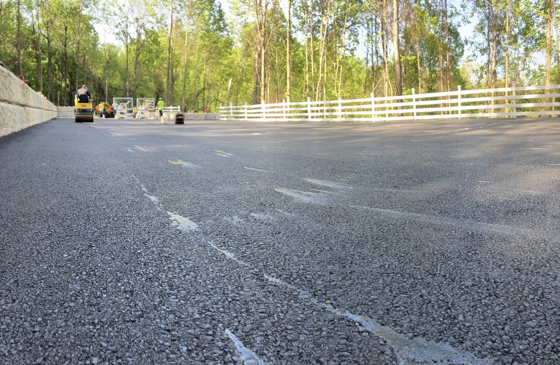 A parking lot with a white fence and trees in the background