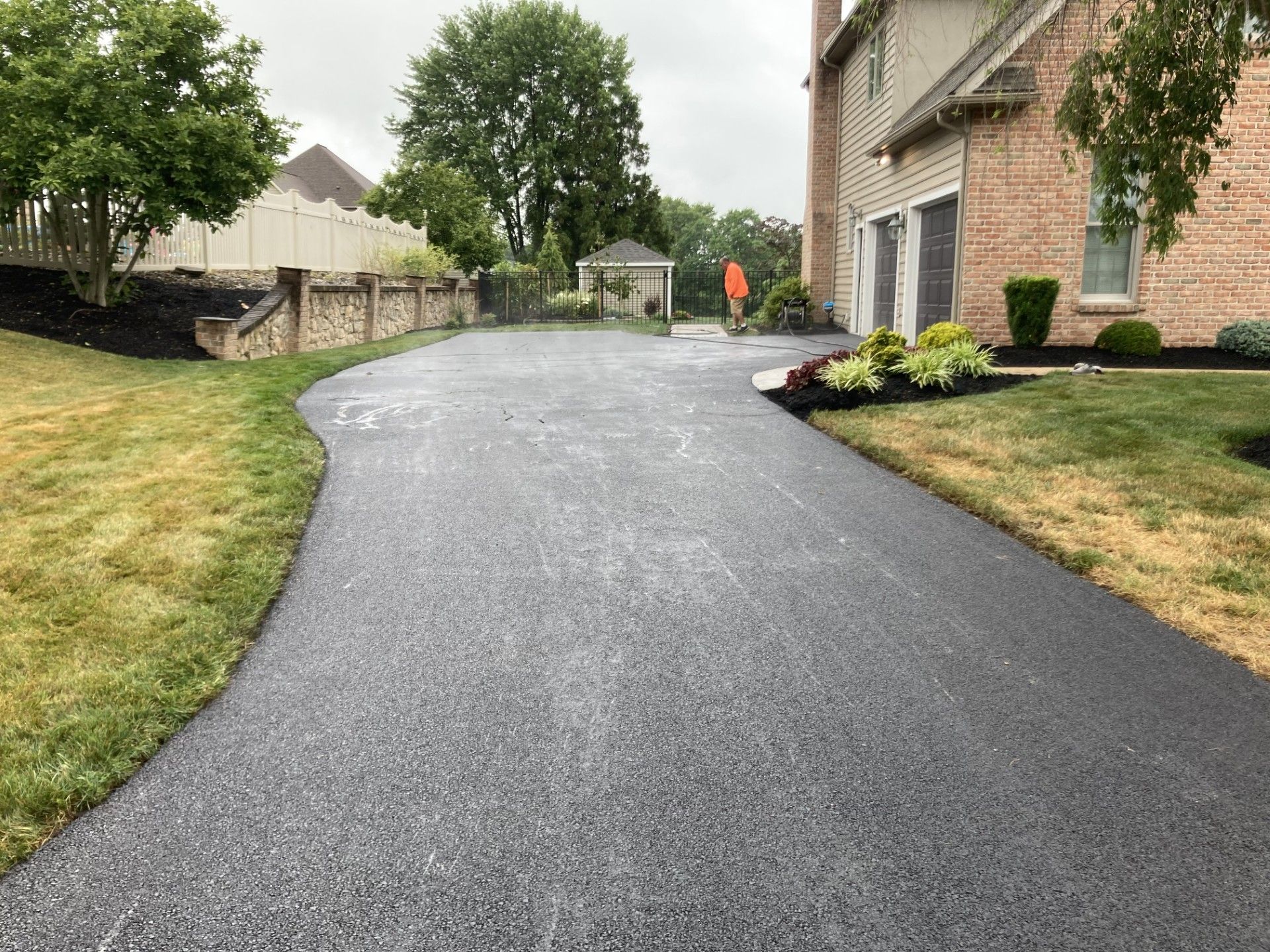 A driveway leading to a house with a brick house in the background.