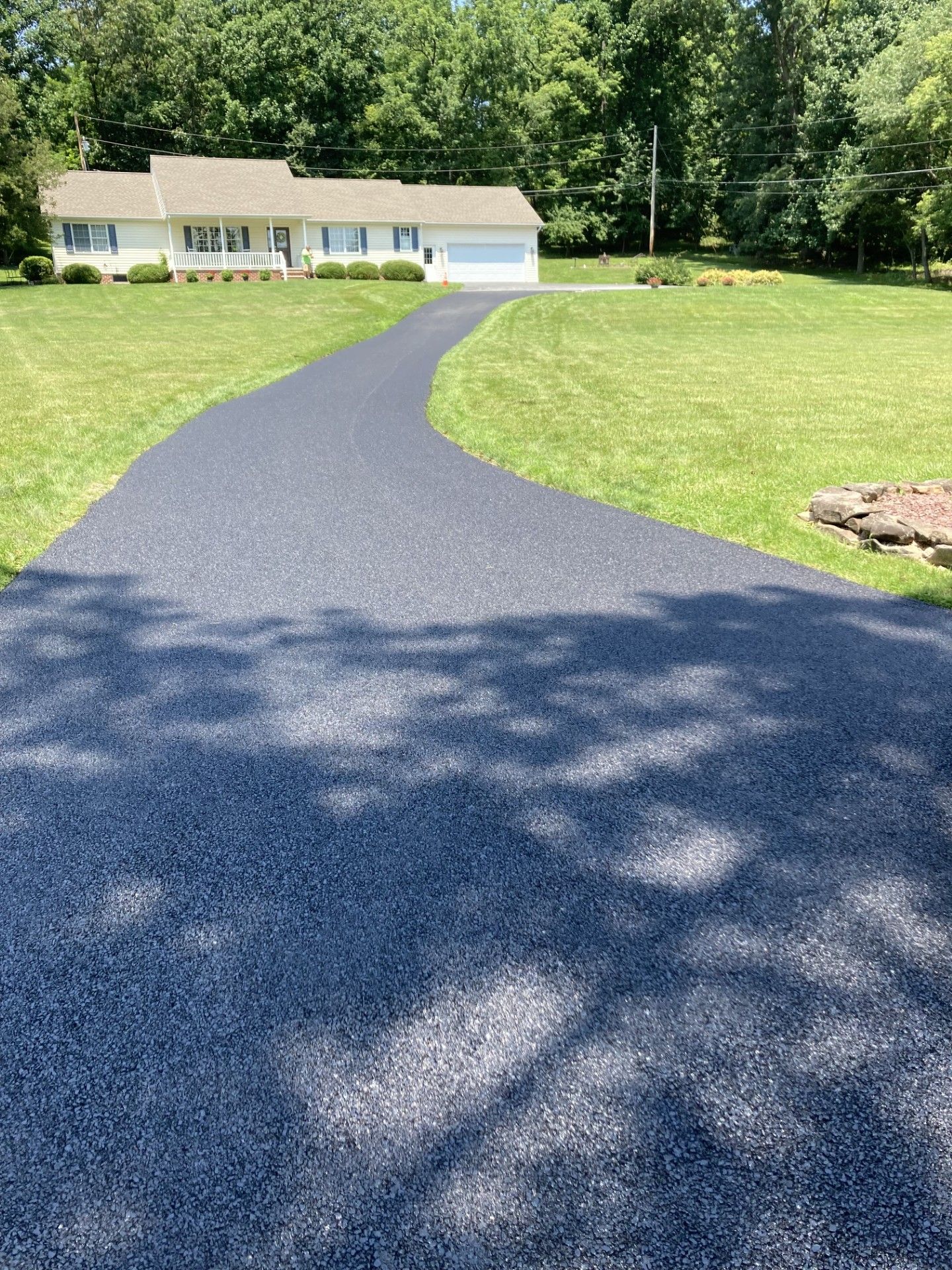 A driveway leading to a house in the middle of a lush green field.